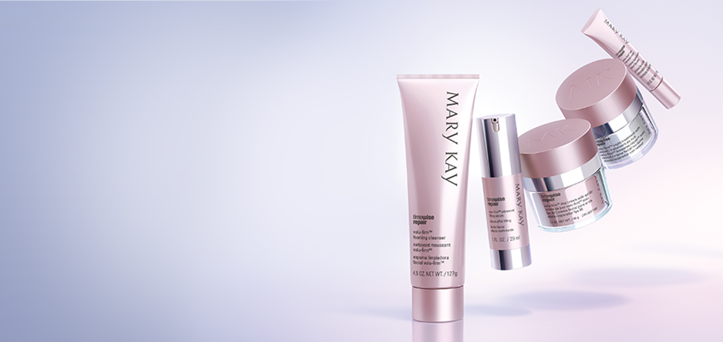 The five products that make up the Mary Kay TimeWise Repair Volu-Firm set, including a cleanser, a serum, a day cream, a night cream and an eye cream, hover in a crescent shape over a purple backdrop.
