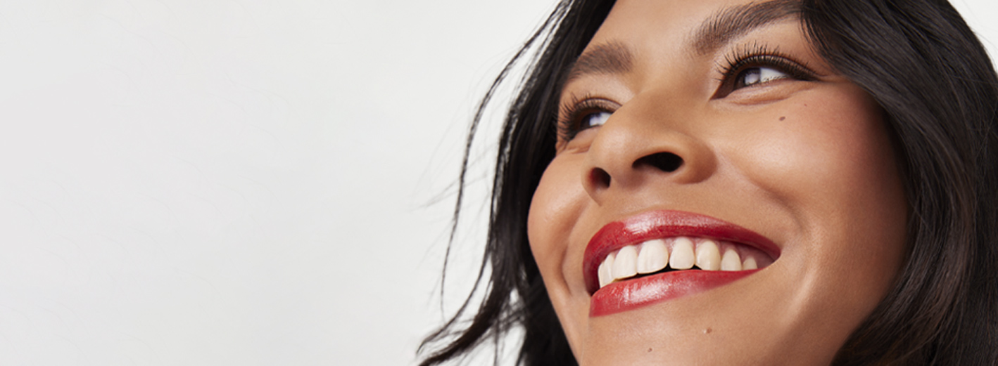 A female model wearing a red lip and mascara appears smiling while looking into the distance.