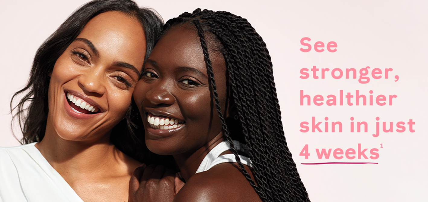 Two black women posing closely together while smiling at the camera surrounded by sunlit lighting and a light pink background