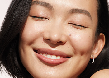 Up close macro image of a brunette Asian woman smiling with her eyes closed surrounded by sunlit lighting