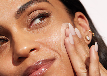 Up close macro image of a black woman confidently looking off to the side while applying skin care to her cheek