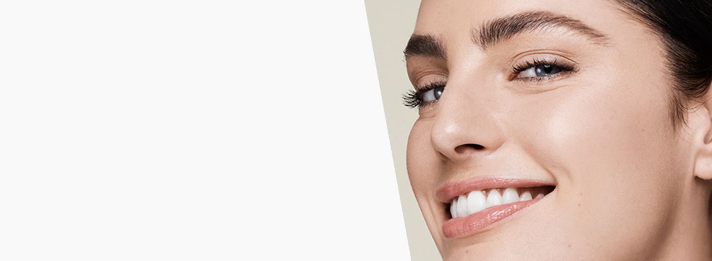 A smiling woman with dark brown hair and beautiful skin on a gray background