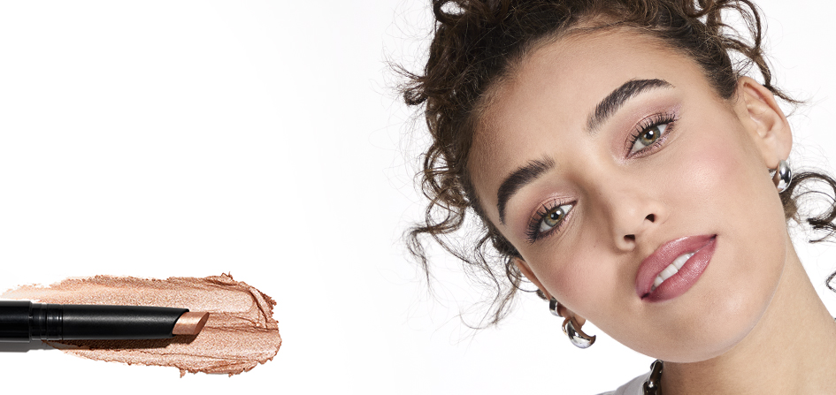 Mary Kay Shimmer Eye Shadow Stick in Golden Sunrise is swatched beneath the open stick and shown alongside a model wearing the shade with a soft, casual expression.