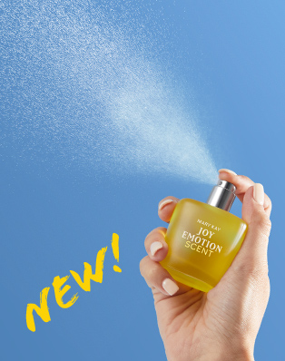 Mary Kay Joy Emotion Scent Eau de parfum yellow bottle held by a hand being sprayed into the air on a blue sky background with the word NEW! in yellow text