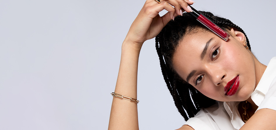 A model with braids holds Mary Kay Unlimited Lip Gloss in shade Cherry Red.