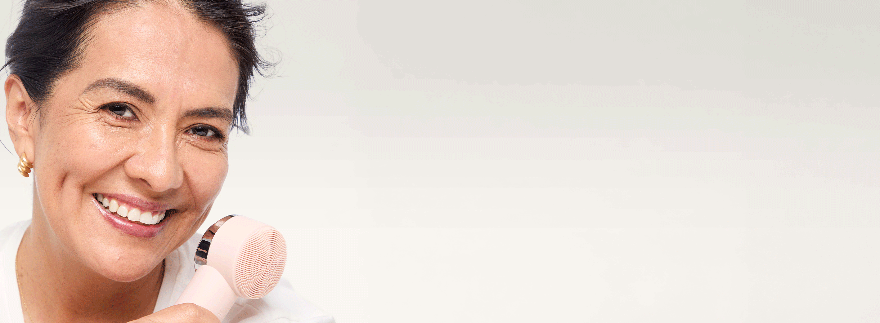 light skinned model with dark hair smiling, holding skinvigorate duo brush